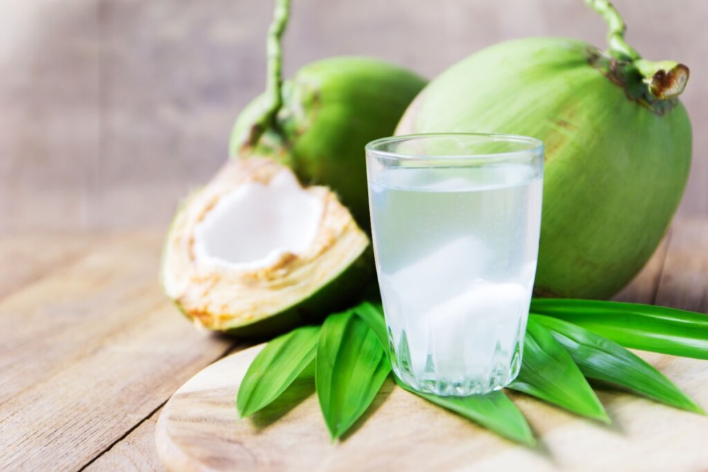 Copo de água de coco fresco ao lado de cocos verdes e folhas em uma mesa de madeira