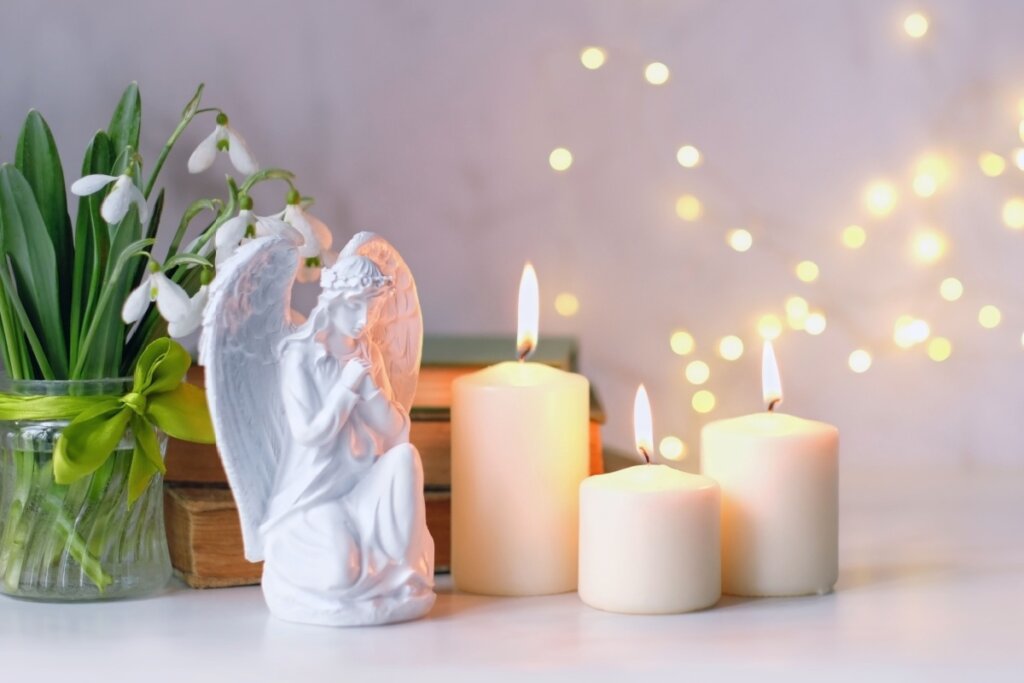 imagem de anjo branco rezando ao lado de três velas brancas acesas