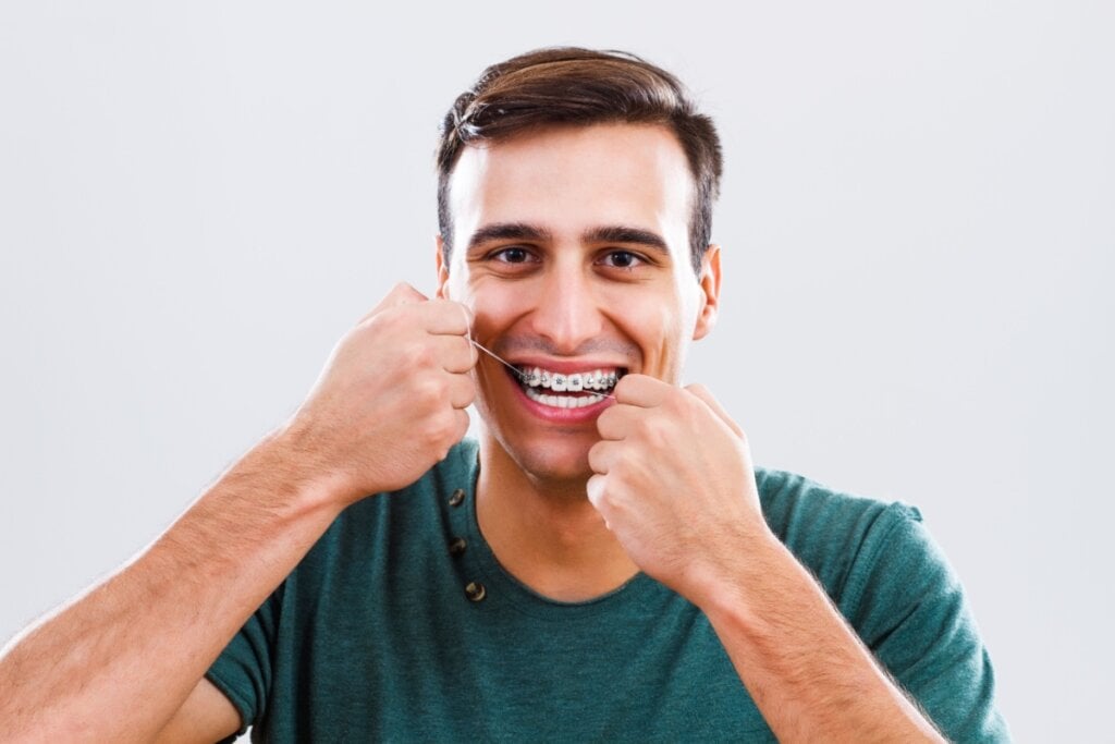 Homem com aparelho ortodôntico passando fio dental nos dentes superiores