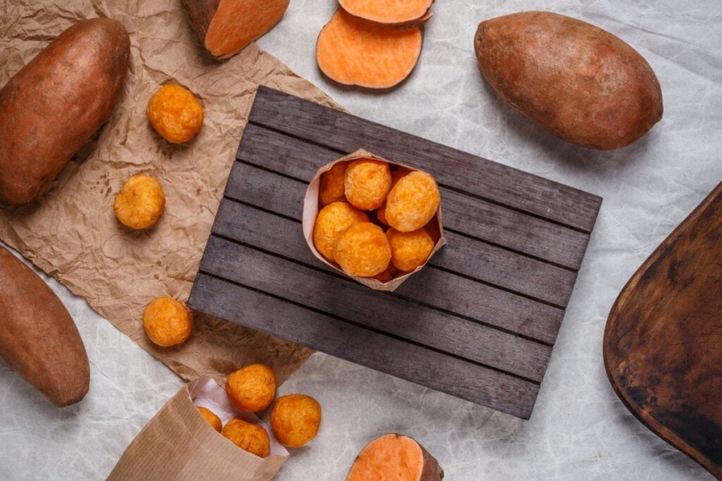 bolinhos de batata-doce dentro de saco de papel e em cima de tábua. batata-doce laranja em volta