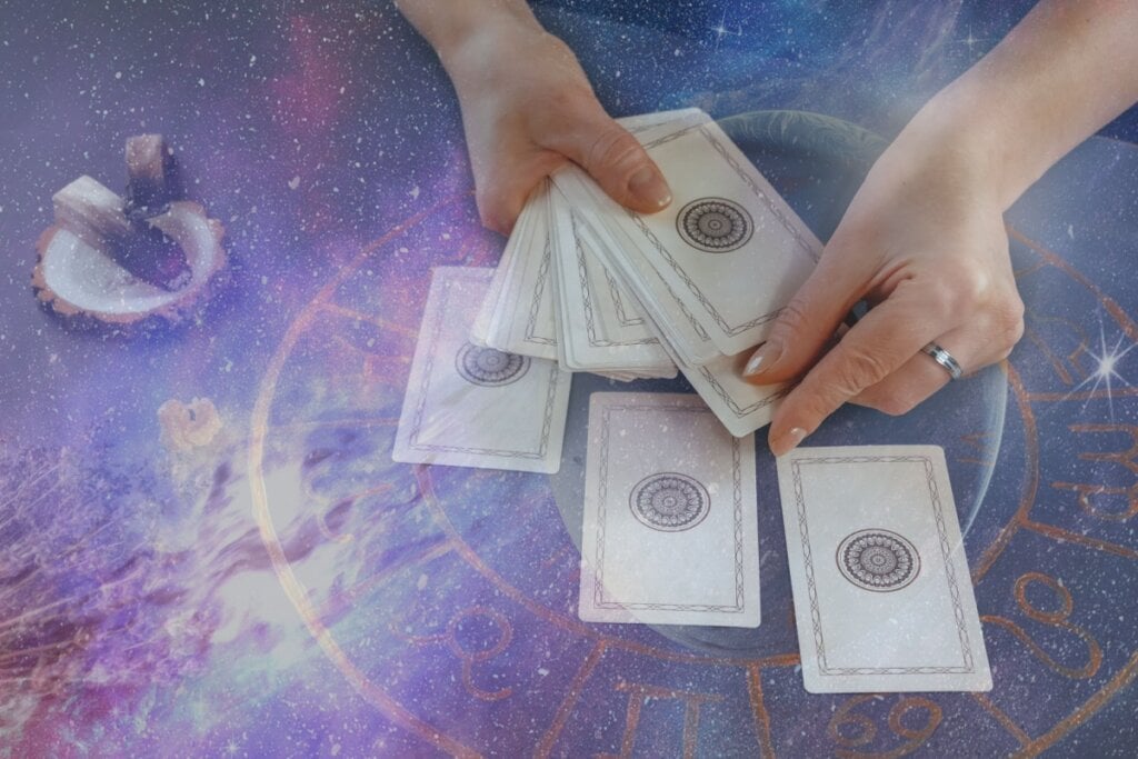 Pessoa mexendo em cartas de tarot com símbolo dos signos na mesa