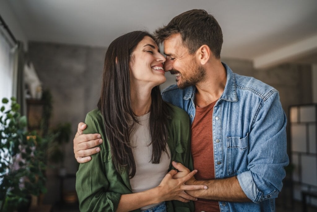 Casal feliz e abraçado com os rostos encostados um no outro.