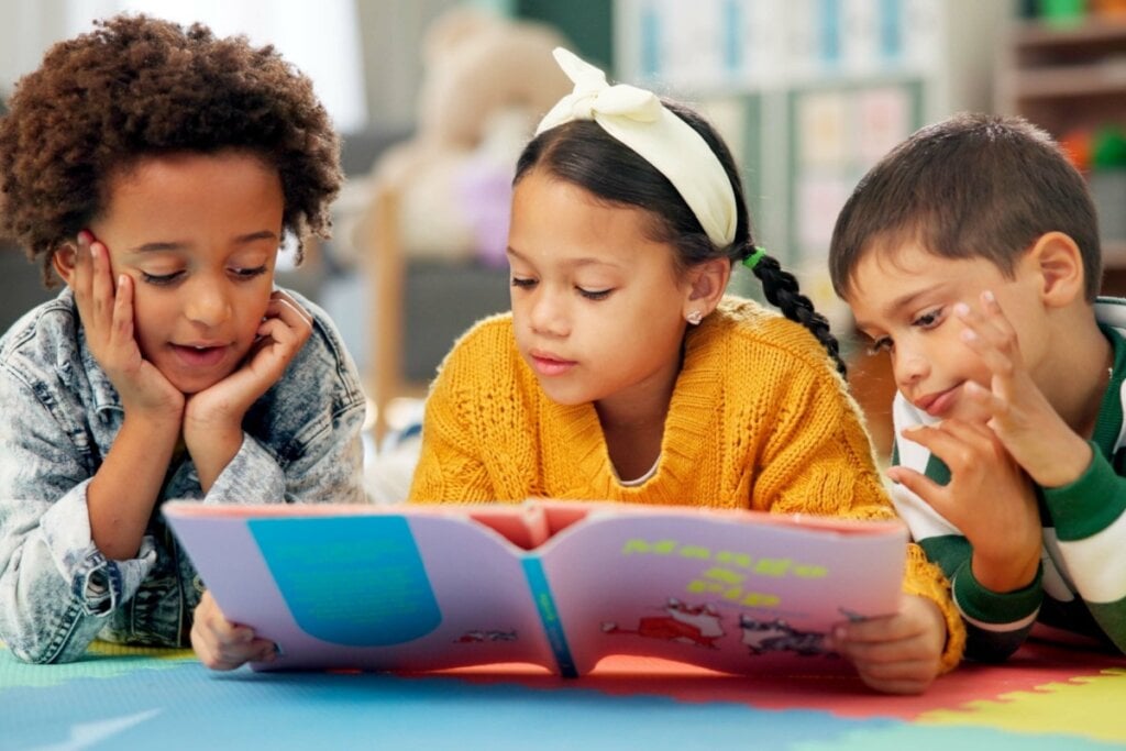 dois meninos e uma menina deitados no chão e lendo livro