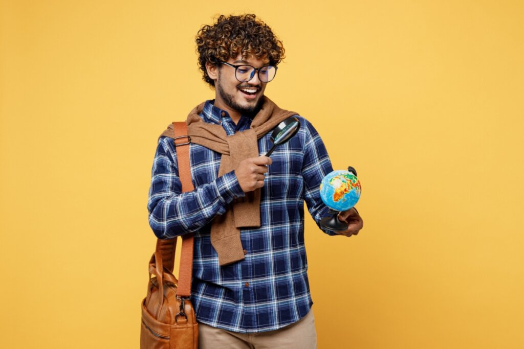 Estudante com o globo na mão apontando uma lupa pra ele