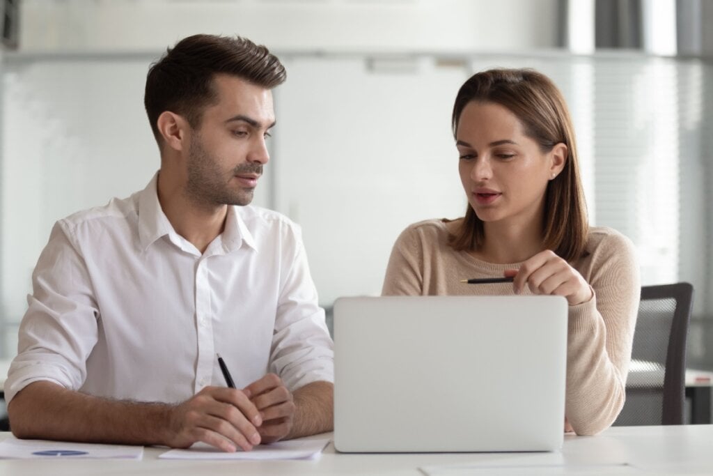 Um homem e uma mulher conversando segurando canetas e manuseando papéis e notebook