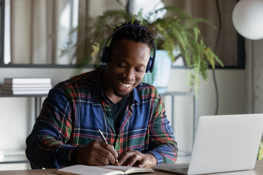 Homem fazendo curso pelo notebook e realizando anotações