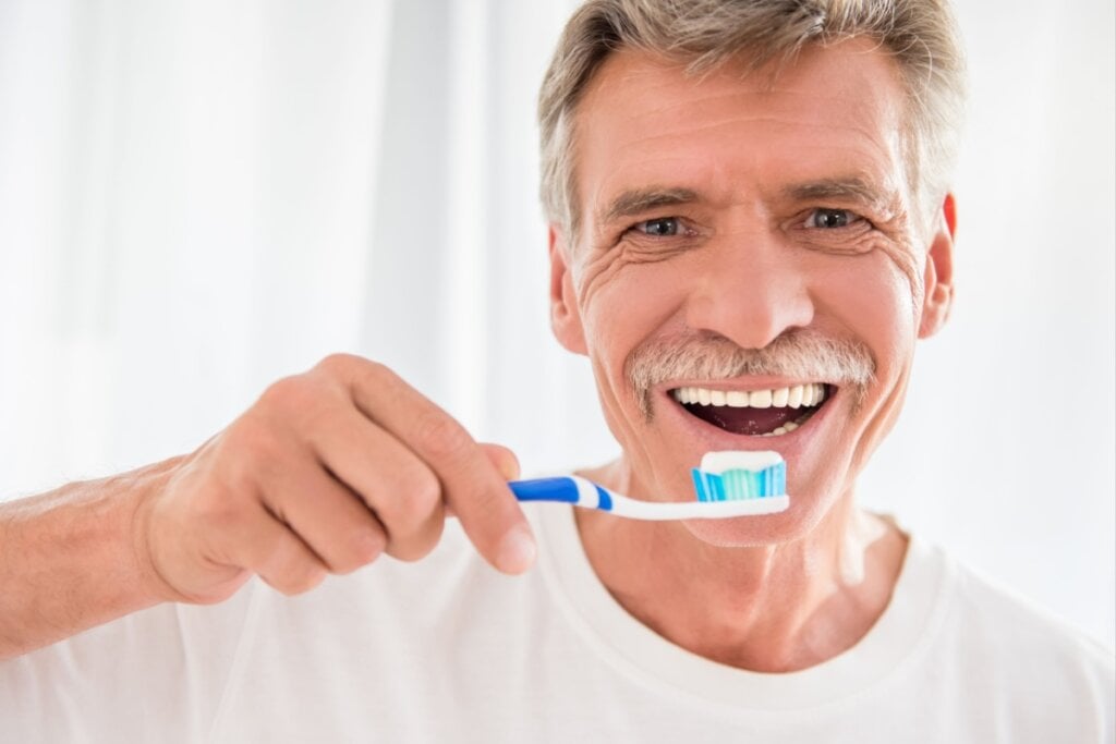 Homem mais velho segurando uma escova de dente com pasta na escova 