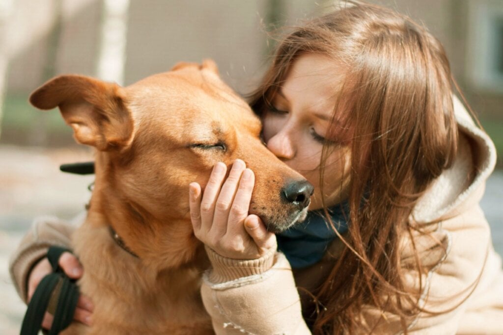 mulher ruiva dando beijo no rosto de cachorro marrom