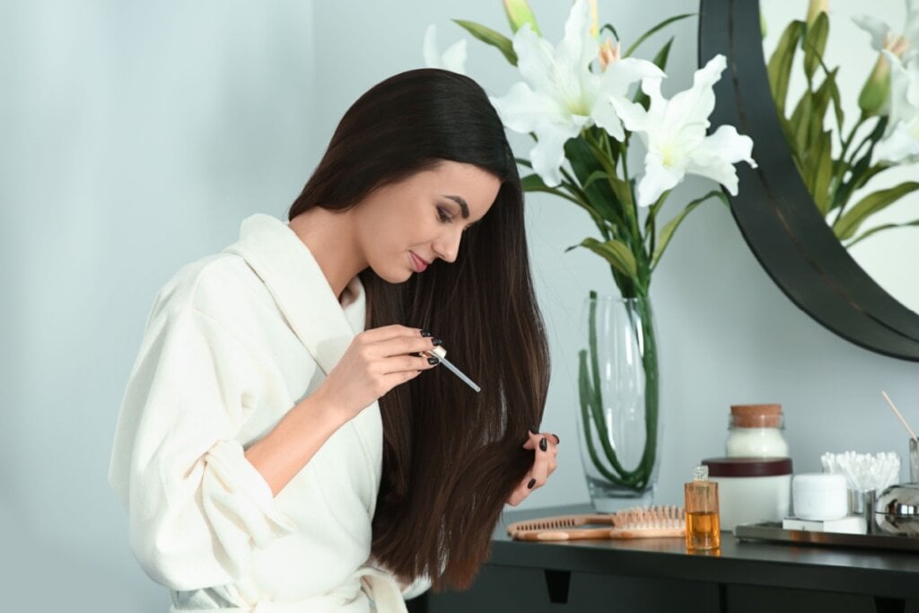 mulher de roupão branco aplicando produto em seu cabelo longo e liso