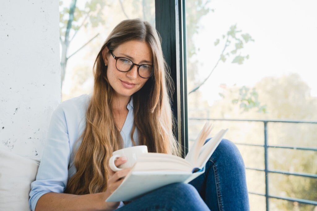 Mulher lendo livro e com uma xícara na mão em um lugar calmo