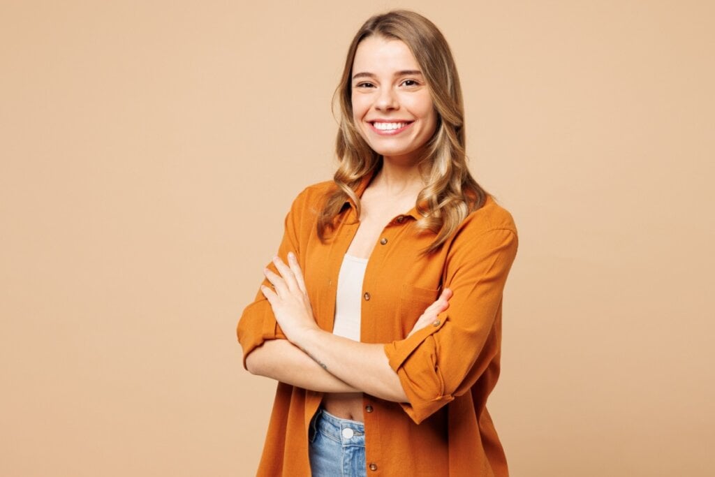 Jovem sorrindo, usando uma camisa laranja e camiseta branca em fundo laranja claro