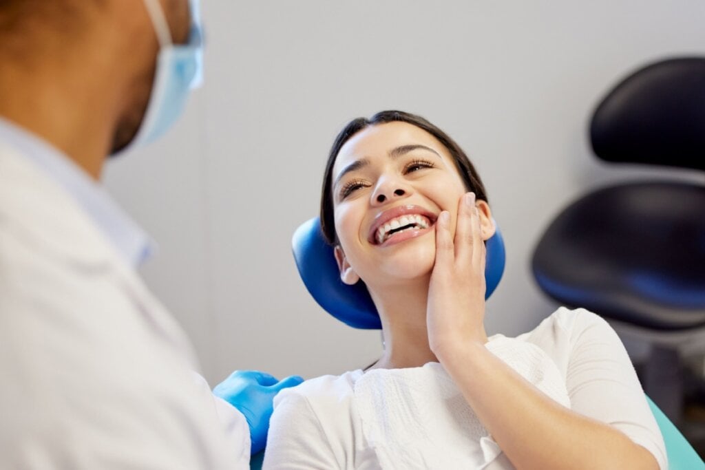 Mulher no consultório do dentista com uma expressão feliz e sorrindo após procedimento de reparação