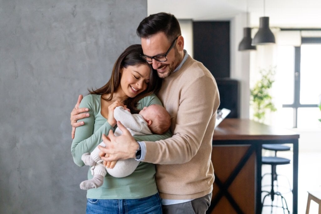 Casal segurando bebe recém-nascido no colo com expressões felizes