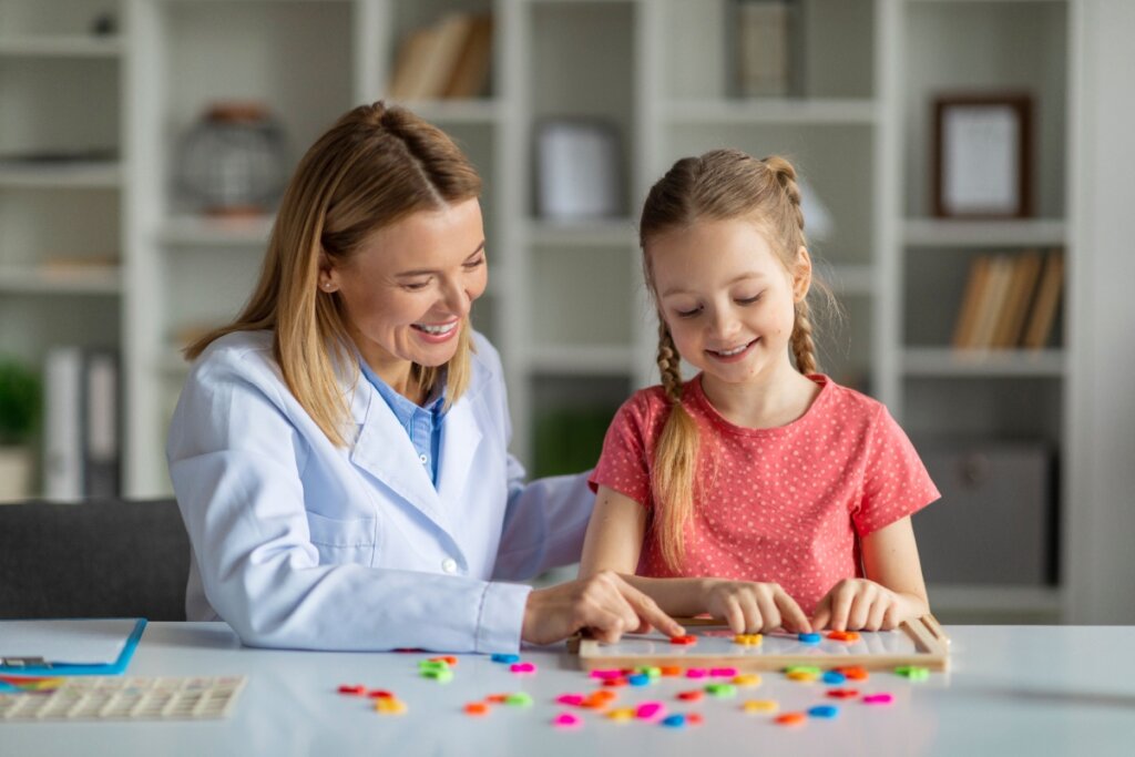 Pedagoga sorridente ensinando uma criança a organizar peças coloridas em uma atividade de aprendizagem sensorial