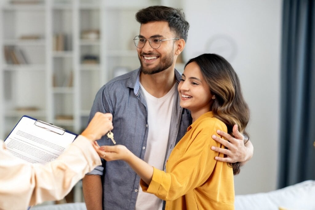 Homem e mulher abraçados pegando uma chave na mão de uma pessoa