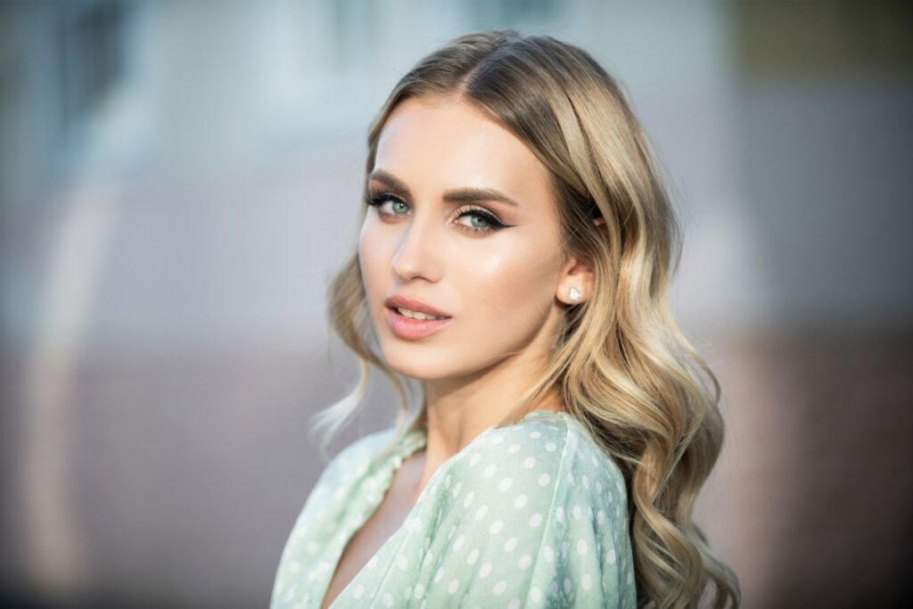 Mulher usando um vestido branco com flores verdes, com o cabelo com ondas solto e olhando para o lado