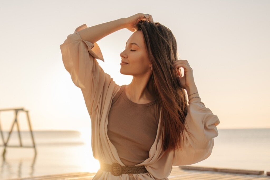 Mulher em frente a um pôr do sol com as mãos no cabelo