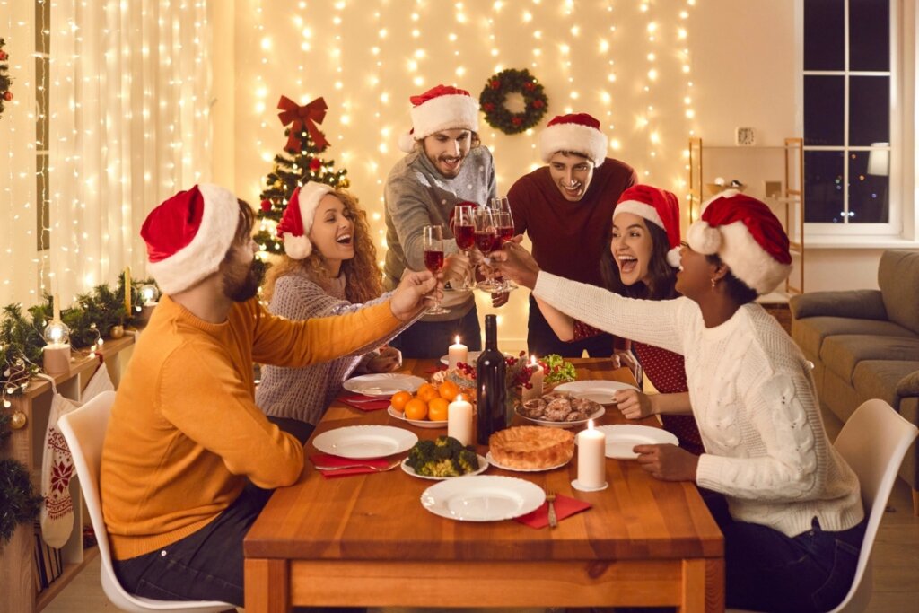 Pessoas reunidas do redor de uma mesa com comidas celebrando o Natal e brindando com taças com vinho tinto