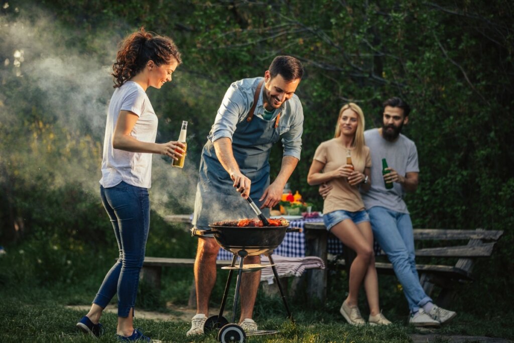 Pessoas reunidas em um jardim com um homem fazendo churrasco