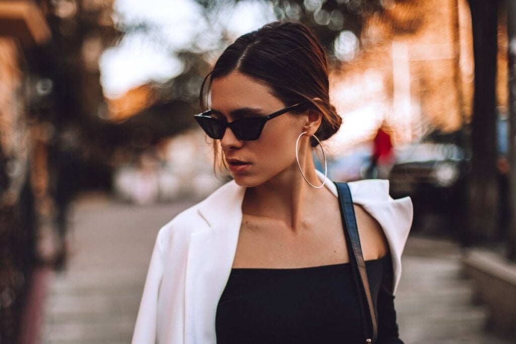 Mulher usando um óculos de sol, com um coque no cabelo e andando na rua 