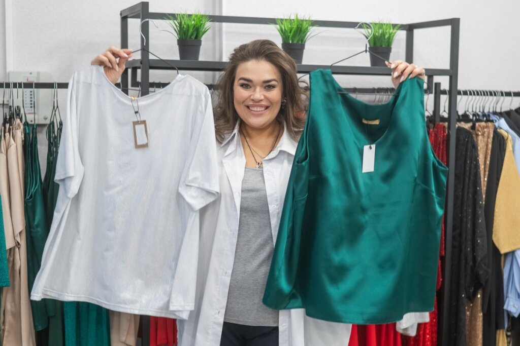 Mulher sorrindo e segurando uma blusa branca e outra verde