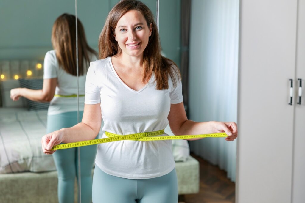 Mulher sorrindo segurando uma fita métrica na barriga