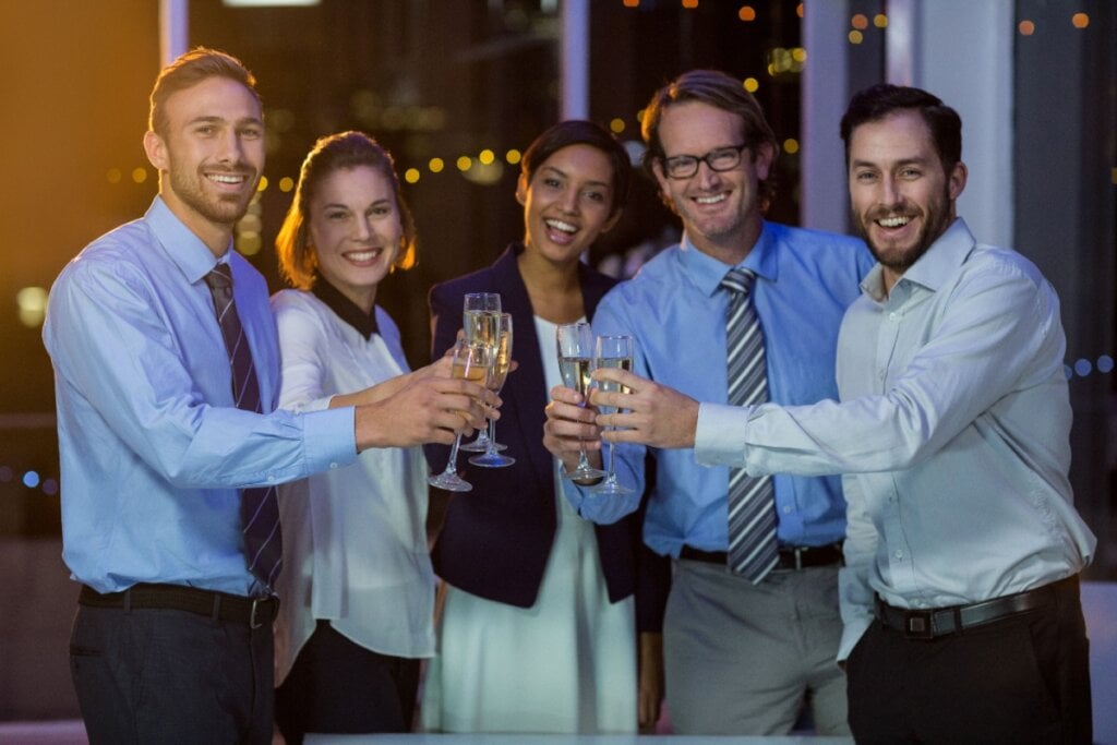 Grupo de colegas sorrindo e brindando com taças em uma festa corporativa