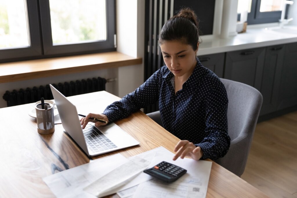 Mulher sentada em uma mesa de escritório mexendo em um computador e em uma calculadora