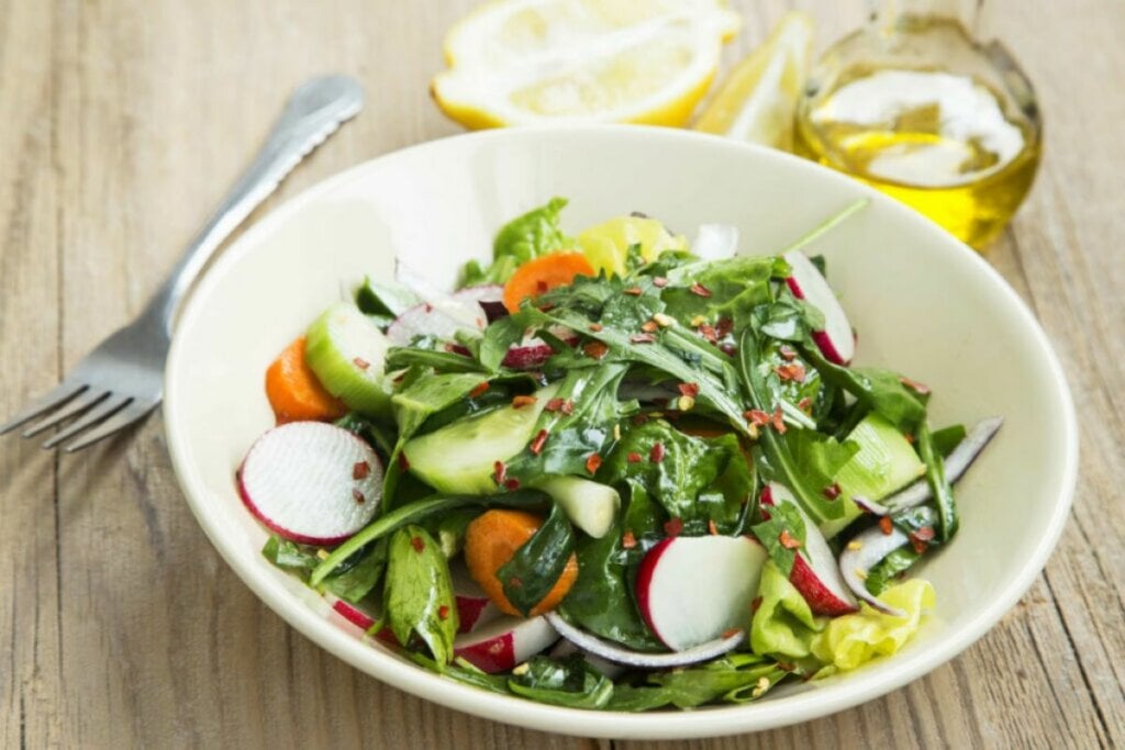 Salada com espinafre, rúcula, alface, rabanete, cenoura, cebola e pepino em um recipiente branco 