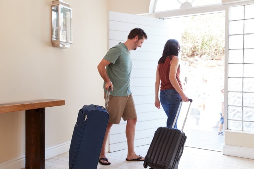 Homem e mulher segurando malas azuis e saindo de uma casa 