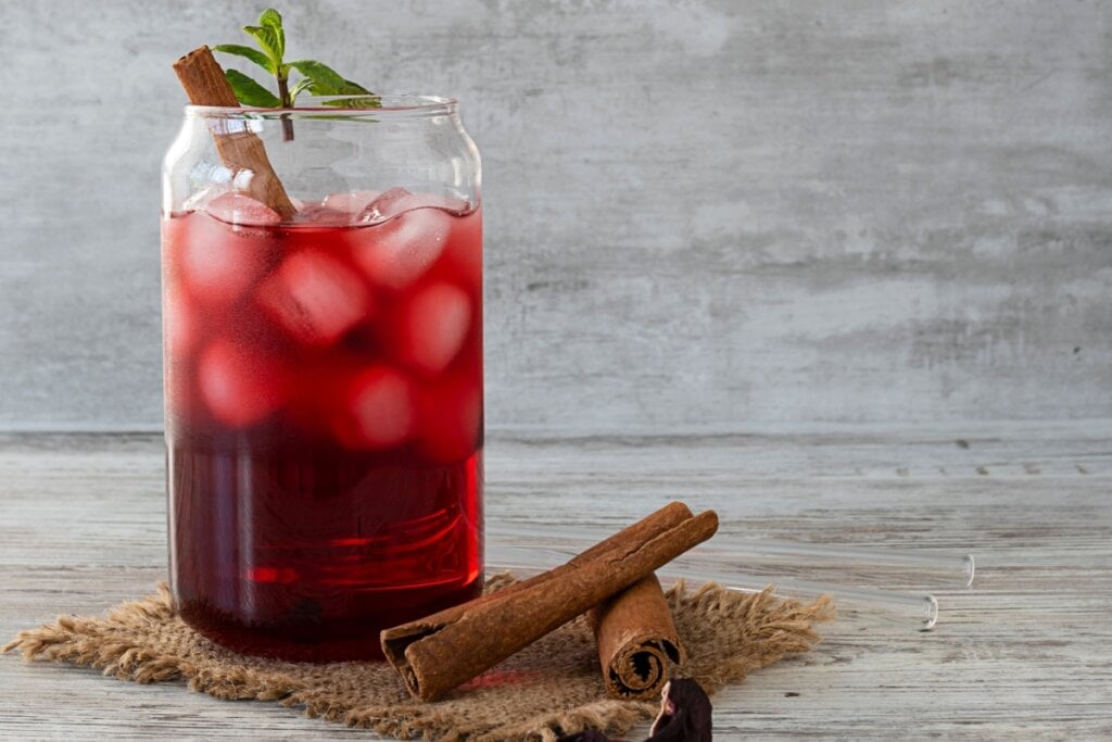 copo de vidro com chá vermelho de hibisco com canela e pedras de gelo