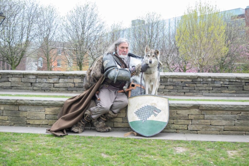 homem vestido como personagem de game of thrones, sentado em muro e segurando cachorro