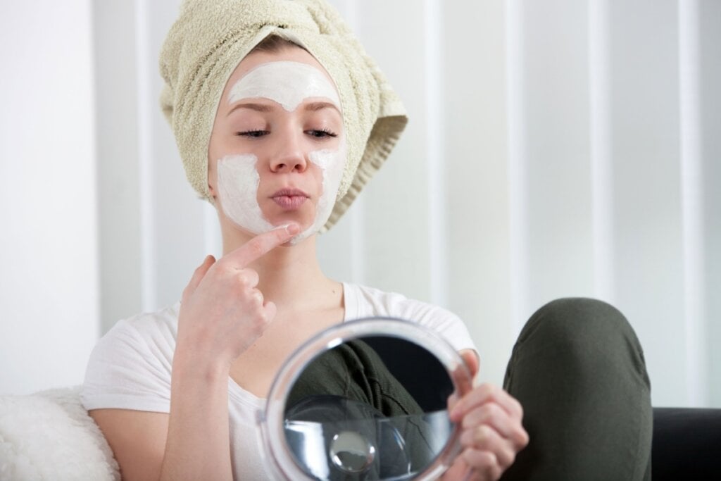 Jovem se olhando no espelho enquanto passa máscara facial