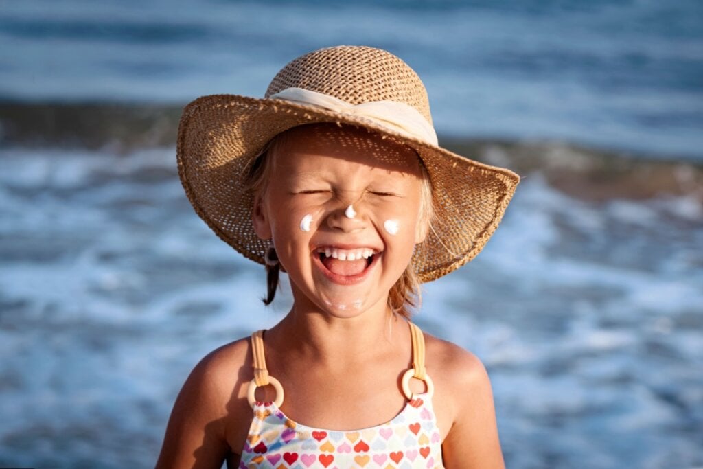 Menina com protetor solar na praia usando chapéu e sorrindo