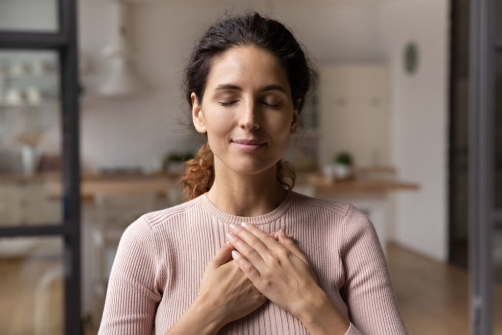 Mulher orando, de olhos fechados e com a mão no coração