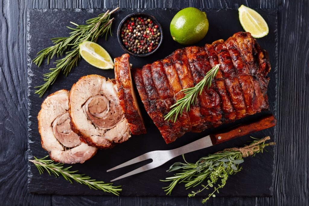 Porchetta acompanhada de ramos frescos de alecrim, limões cortados e grãos de pimenta colorida