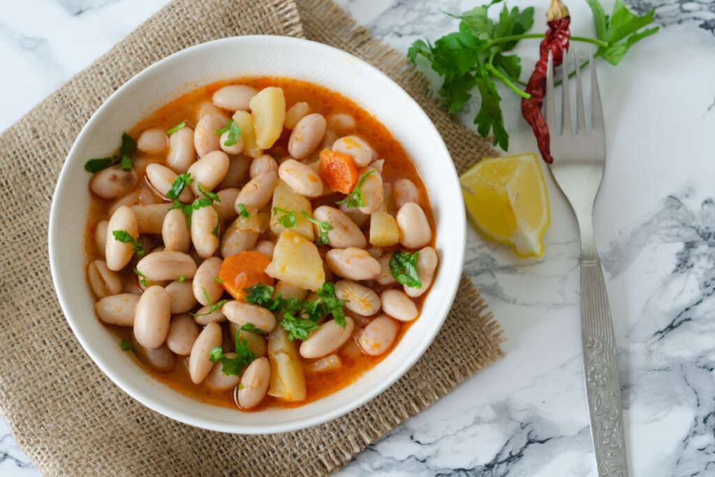 sopa de feijão-branco com cenoura e batata em prato branco com limão e garfo ao lado