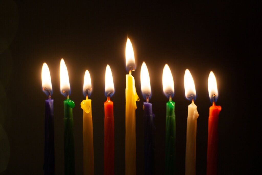 9 velas coloridas e acesas nas cores roxo, verde, amarelo e vermelho.