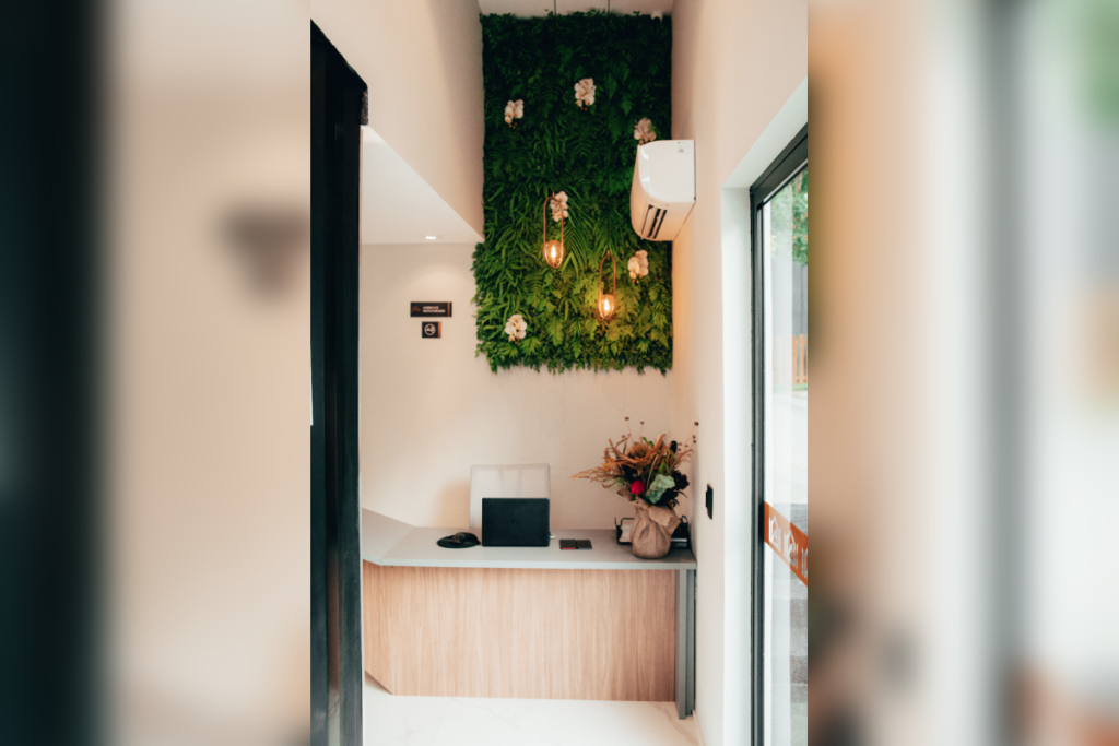 Hall de entrada decorado com parede vertical de plantas, iluminação suspensa e uma mesa de recepção minimalista