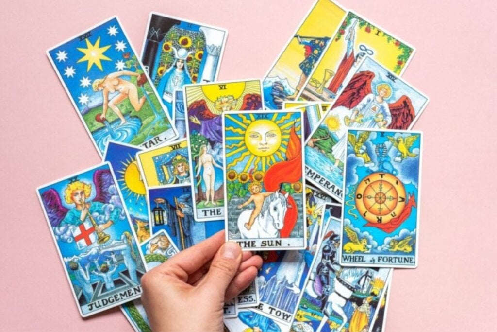 cartas do tarot em fundo rosa. mão segurando arcano do sol