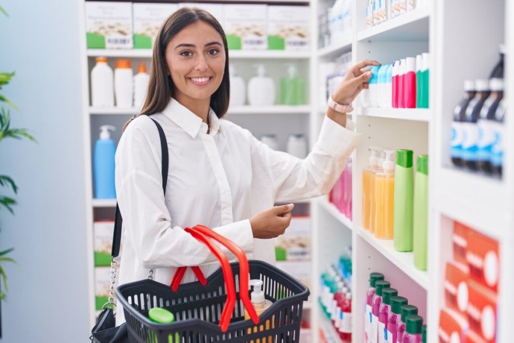 Mulher sorrindo e segurando uma cesta com produtos em uma farmácia