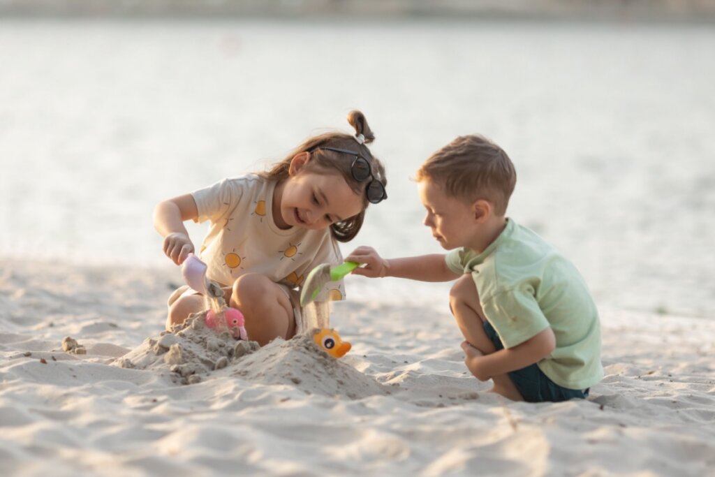 menino e menina brincando de cobrir brinquedo com areia na praia