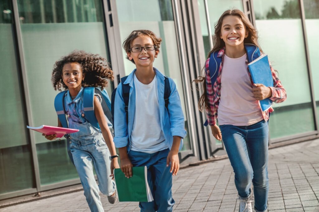 Três crianças chegando na escola, duas meninas e um menino.