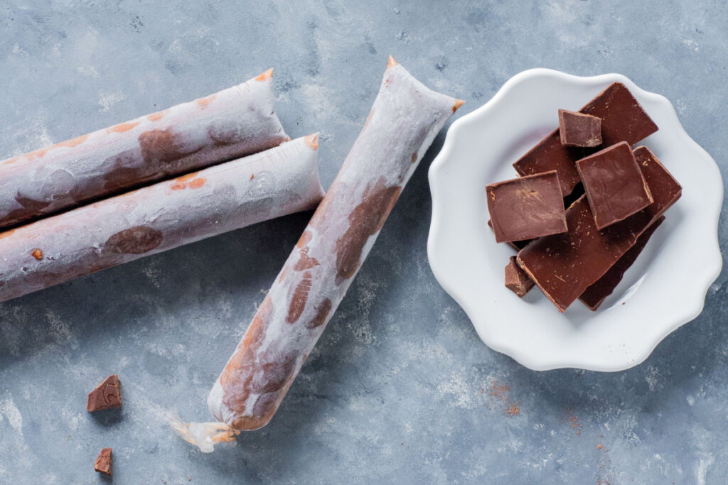 três geladinhos e chocolate ao lado de prato branco com chocolate