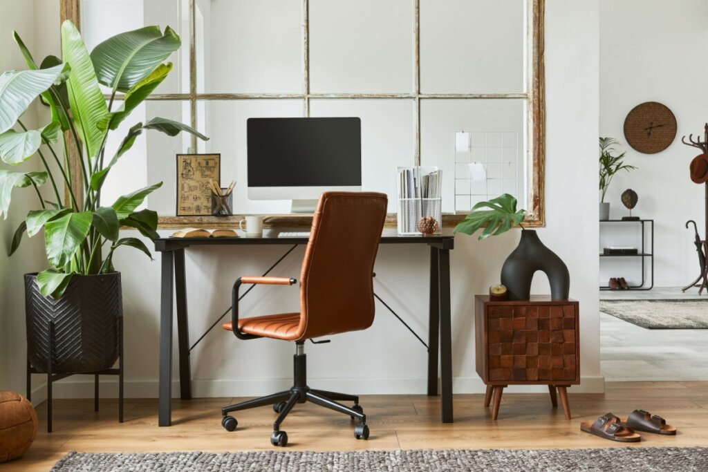 imagem de home office com cadeira marrom, mesa com computador e plantas ao lado