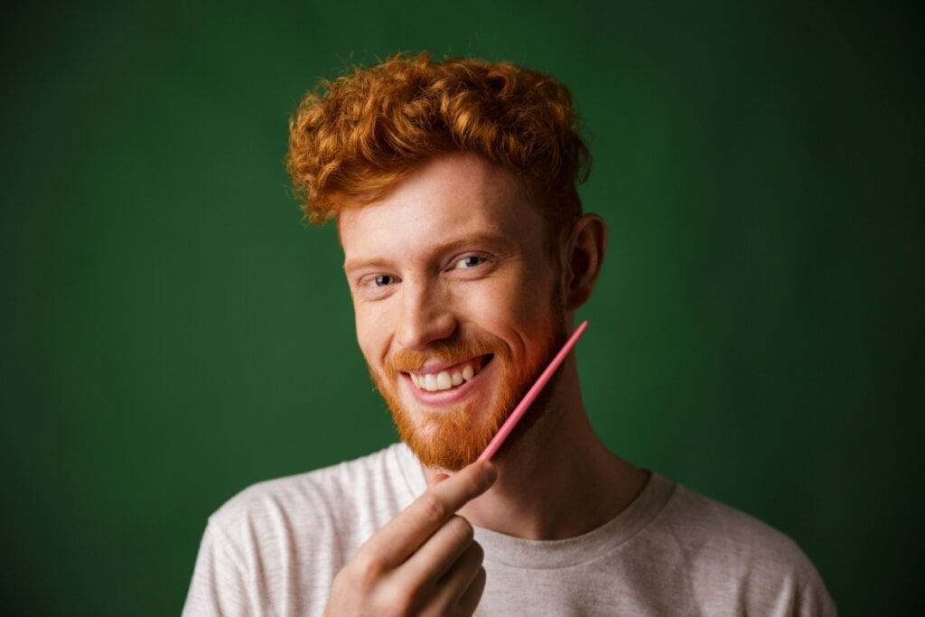 Homem ruivo penteando a barba em um fundo verde-escuro