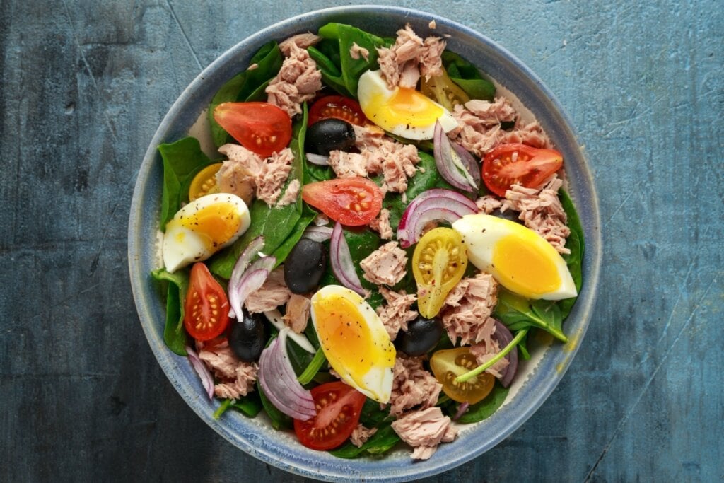 Salada de atum, espinafre e ovo servido em tigela de cerâmica azul em cima de mesa de madeira