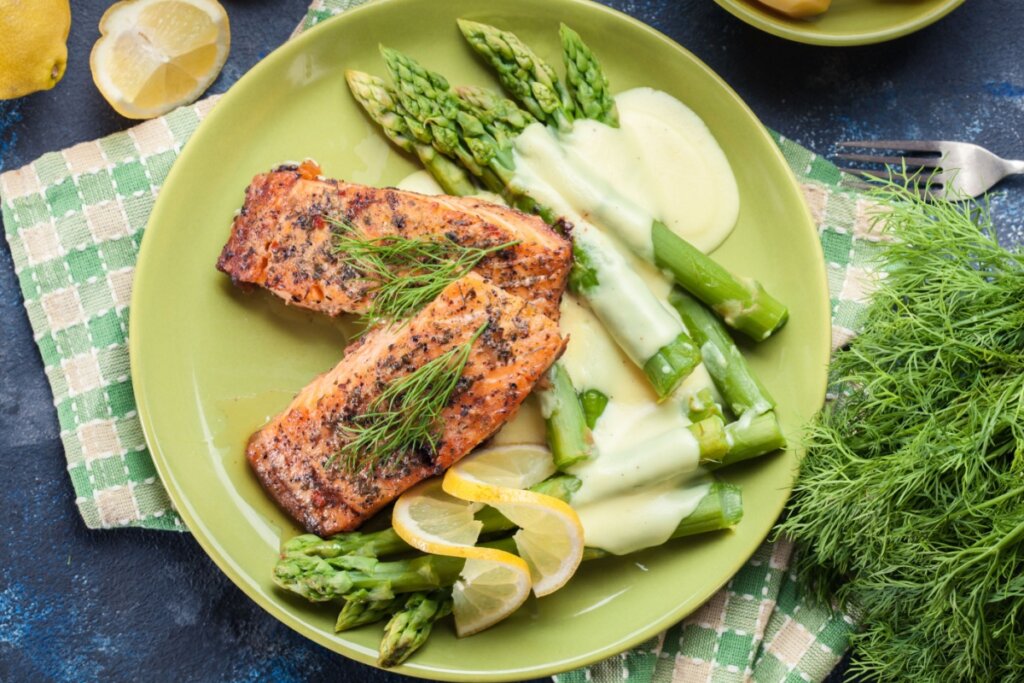 prato verde com dois pedaços de salmão, aspargos e molho amarelado